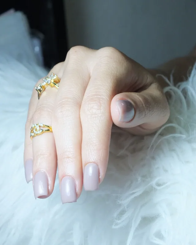Mão em repouso com unhas em tom nude sobre superfície clara